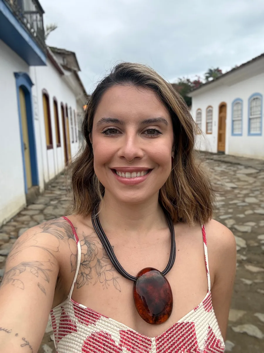Retrato de Layana Belyssa sorrindo em uma rua de pedras com casarios coloniais ao fundo